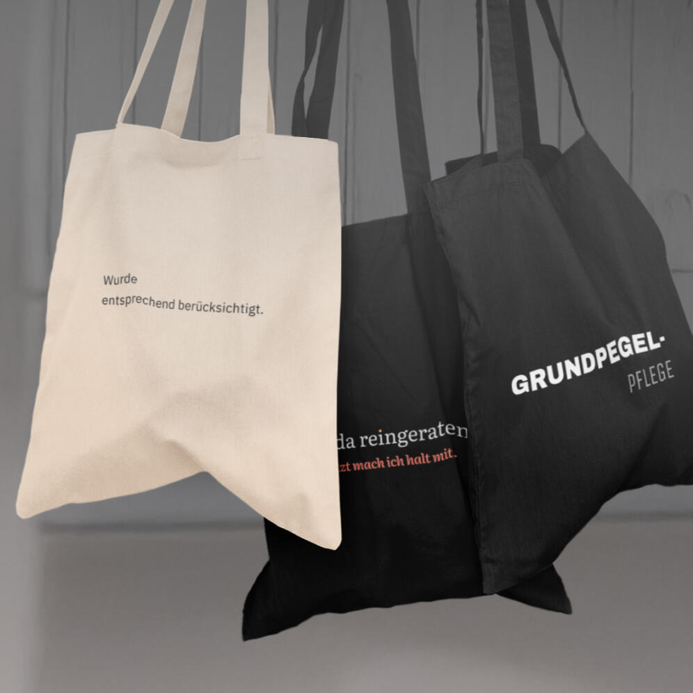 Stoffbeutel mit mehreren Arbeitssprüchen in schwarzem und beigem Design, hängend an einer Garderobe.